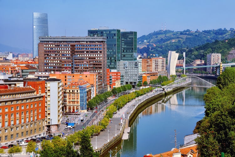 Photo of aerial view of Bilbao, Spain city downtown with a Nevion River, Zubizuri Bridge and promenade. Mountain at the background.