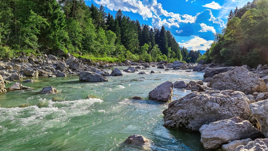 River Gail flowing through the Schuett in the natural park Dobratsch in Villach, Carinthia, Austria. Gailtaler and Villacher Alps. Riverbank is full of massive rocks. Swimming in crystal clear water