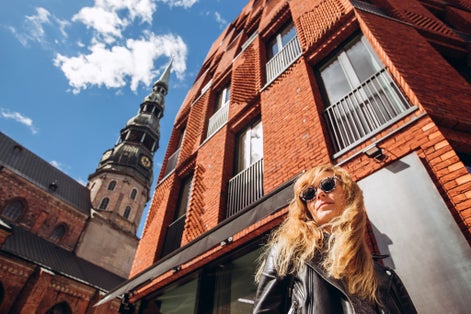 photo of tourist girl in glasses walks through the old Riga. Portrait of a young female tourist in front of st. peter's church in Riga. Women have a great holiday in Latvia.
