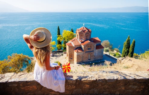 Photo of woman in white dress and Macedonian flag enjoying Ohrid lake, North Macedonia.