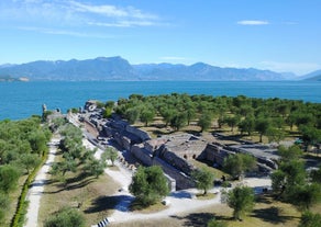 Photo of Old harbour Porto Vecchio with motor boats on turquoise water, green trees and traditional buildings in historical centre of Desenzano del Garda town, Northern Italy.