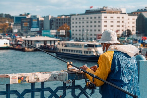  Elder man wearing colorful raincoat fishing at Galata Bridge in Golden Horn, Istanbul. Rod fishing from Galata Bridge very popular.