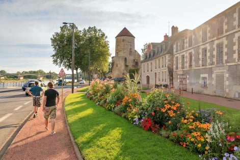 Photo of tourists walking on the boulevard of Nevers on a summer afternoon at the river Loire with vibrant flowers and the Goguin Tower, France.