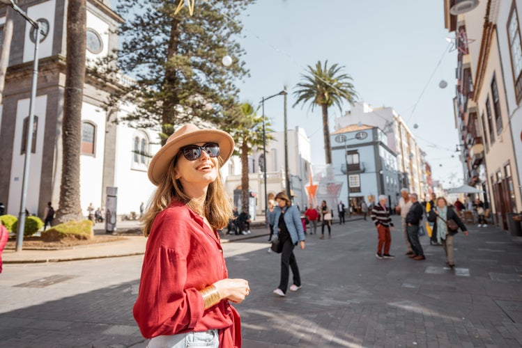 Portrait of a young and happy woman walking on the street with beautiful spanish colonial buildings at the old town of La Laguna city, traveling on Tenerife island