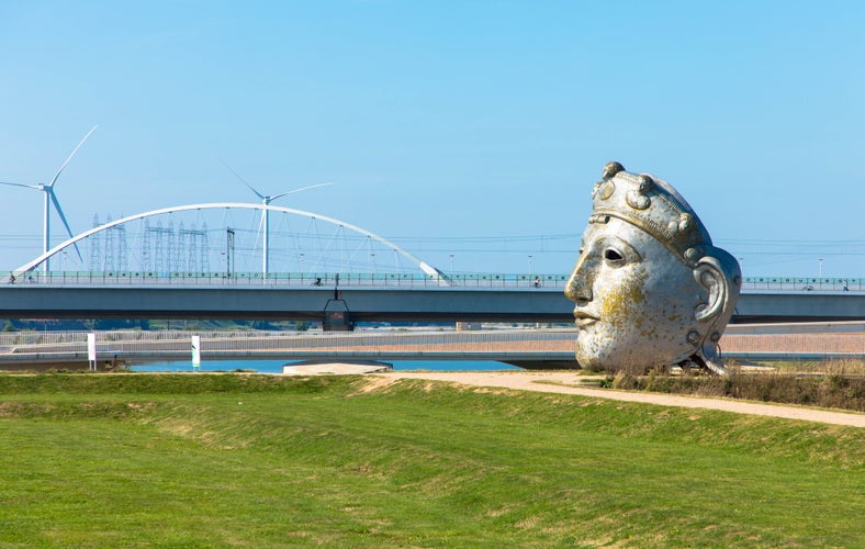 Huge replica of a Roman mask on the banks of the Waal with the Lentloper Bridge in the background. It is called the face of Nijmegen. Oosterhoutsedijk Gelderland, Netherlands