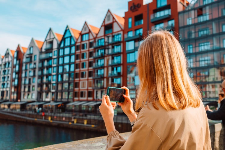 Photo of view of lady tourist takes photo or video on smartphone at city of Gdansk, Poland.