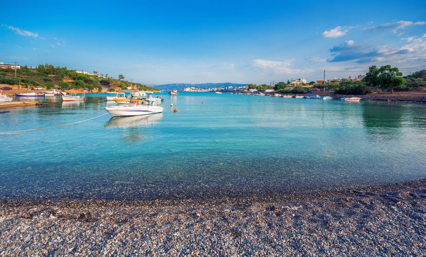 Photo of beach and small natural harbor with anchored fishing boats with the beautiful town of Agios Nikolaos at the background, Crete, Greece.