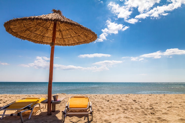 Photo of straw umbrella with deck chairs on a sandy beach by the sea. The Paralia, a tourist seaside part of the municipality Katerini, Greece.