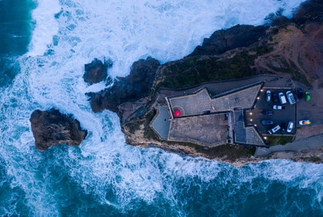 Bird`s eye view of Nazaré light tower and strong waves breaking on the rocks during sunset