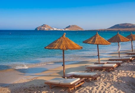 Photo of the sandy beach near the blue sea with sun beds and umbrellas, Mykonos, Greece.