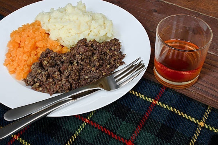 A traditional Scottish Burns Supper featuring haggis, neeps (turnips), and tatties (potatoes), served alongside a glass of whisky.jpg