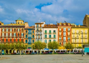 Photo of aerial view of Bilbao, Spain city downtown with a Nevion River, Zubizuri Bridge and promenade. Mountain at the background, with clear blue sky.