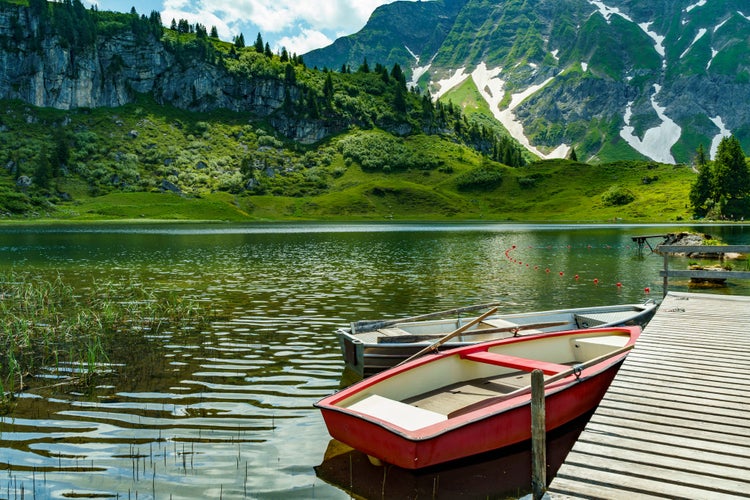 Rowing boats on the Körber lake in the mountains of the Bregenz Forest. anytime changing weather with sun and clouds illuminate the flowered meadows from three stage alpine farming around the lake