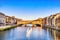 photo of golden sunset over ponte vecchio bridge with traditional boat on the arno river, Florence, Italy.