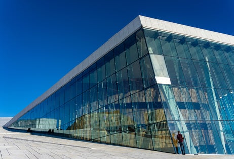 Photo of cool and futuristic opera house on the water under a bright blue sky, Norway.