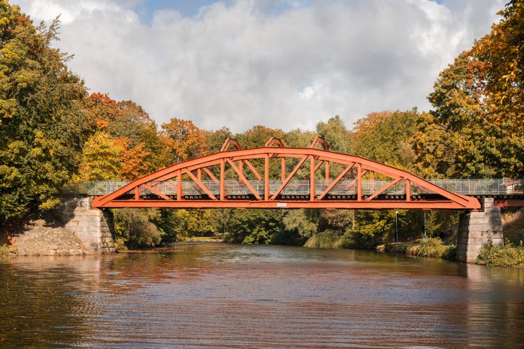 photo of view of Autumn colors surrounds the red bridge Pyttebron over Ronne river which is built 1904 and still in use today in Angelholm, Sweden.