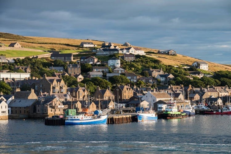 Stromness village in the Orkney Islands, Scotland, with its charming stone buildings lining the waterfront and small boats in the harbor under a cloudy sky..jpg