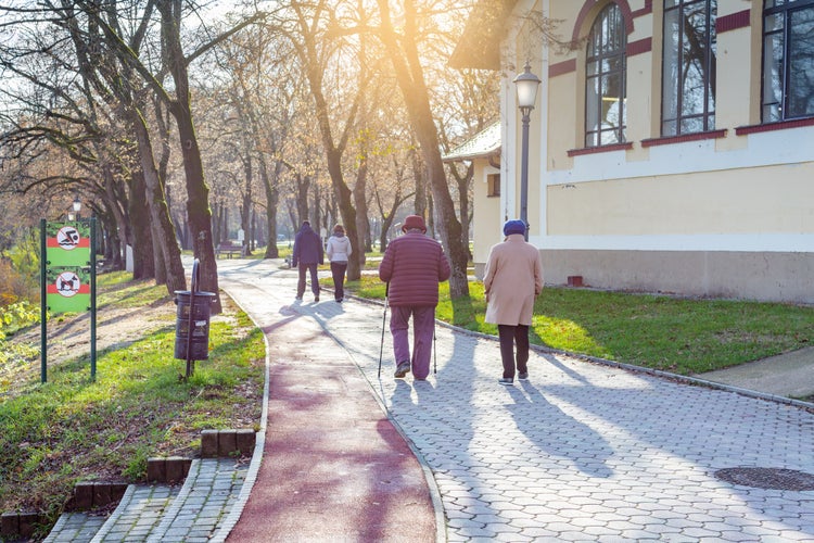 Elderly women and young couple walk along the park path. One of the women using nordic walking poles. Nyiregyhaza, Hungary