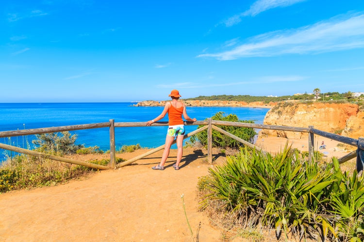 Photo of tourist standing on cliff and looking at beautiful sea coast, Portimao town, Portugal