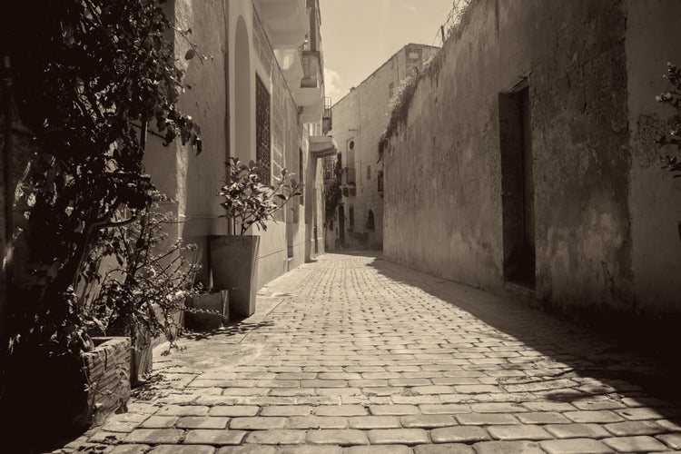 photo of view of A typical old narrow street in Birkirkara, Malta featuring old houses in sepia and monochrome.