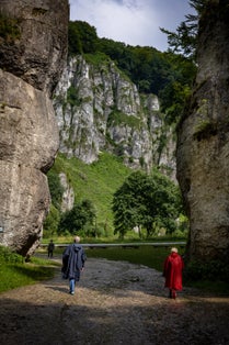 A couple in storm coats walking through a rock gate. A picturesque limestone rock formation called "Cracow gate“. Ojcow, Polish Jura, Poland.
