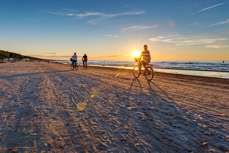 Empty Jurmala beach with lonely girl figure by bicycle, sun in a bicycle basket. Serenity concept. Scenic evening seascape