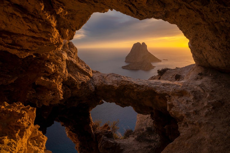 Es Vedra islet at sunset viewed through the rock holes of a cave in Ibiza.jpg