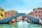 Stone bridge Ponte di Vigo across Vena water canal with colorful boats and old buildings in historical centre of Chioggia town, blue sky background in summer day, Veneto Region, Northern Italy