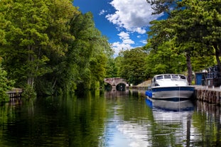 Photo of a narrow boat moored at the river Gade, Grand Union Canal. The Grove Bridge aka Grove Ornamental Bridge No 164 is in the background, Cassiobury Park, Watford, England.