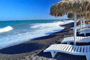 Photo of aerial view of black Perissa beach with beautiful turquoise water, sea waves and straw umbrellas, Greece.