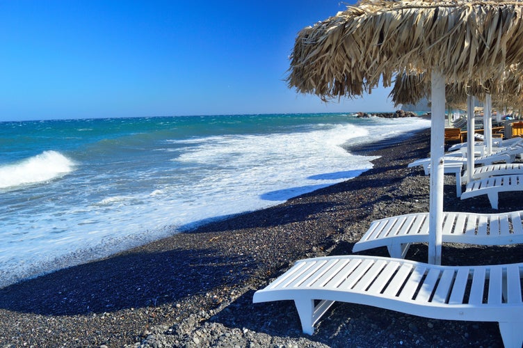 Photo of sunbeds and unique black volcanic pebble beach in Kamari, Santorini.