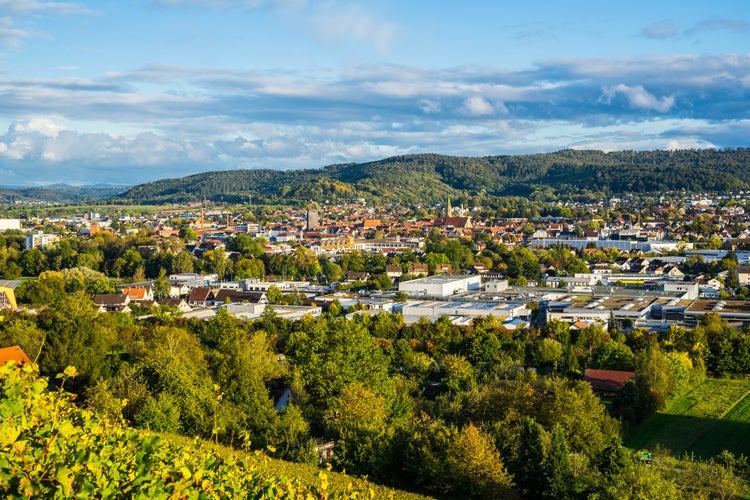 Germany, Wide aerial view above houses, church and roofs of schorndorf city in valley between forested hills in warm evening sunset light