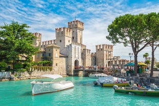 Photo of Old harbour Porto Vecchio with motor boats on turquoise water, green trees and traditional buildings in historical centre of Desenzano del Garda town, Northern Italy.