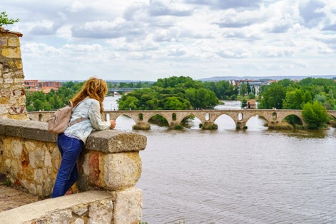 photo of woman looking at the river and Puente de Piedra in Zamora, Spain.