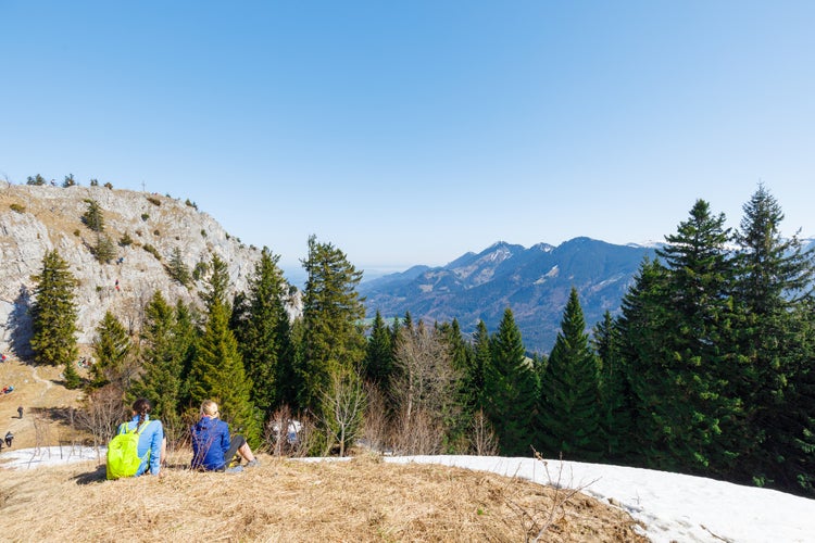 two young women sitting summit of partly snow covered Mountain Heuberg, Nussdorf, Rosenheim, enjoying spring time, Bavaria