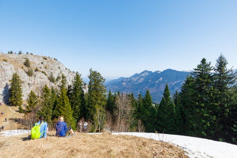 two young women sitting summit of partly snow covered Mountain Heuberg, Nussdorf, Rosenheim, enjoying spring time, Bavaria