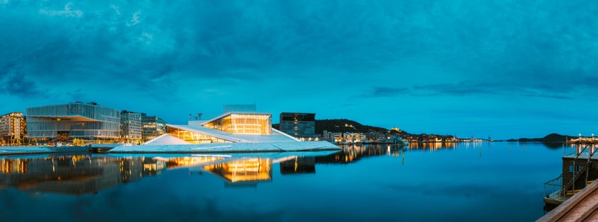 Oslo, Norway. Scenic Night Evening View Of Illuminated Norwegian National Opera And Ballet House Among Contemporary High-Rise Buildings. Panorama, Panoramic View.