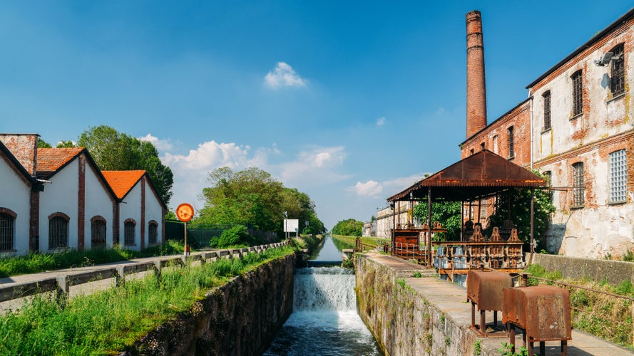 Old industrial warehouses alongside a cascade on a lock at the Naviglio Pavese, a canal that connects the city of Milan with Pavia, Italy