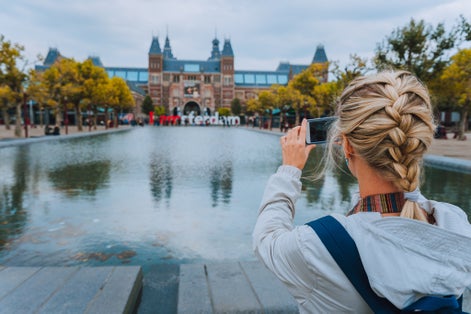 photo of woman tourist taking photo of the Rijksmuseum in Amsterdam on the mobile phone. Travel in Europe city trip concept.