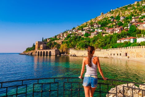 Photo of tourist woman look on ancient shipyard from Kizil Kule tower with beach view in Alanya peninsula, Antalya district, Turkey.