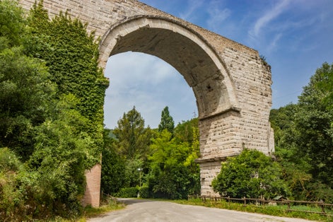 The ruins of the Roman arch bridge of Augustus, in Narni, Terni, Umbria. The remains of the bridge over the Nera river. The big and ancient stone arch, against the blue sky. Trees and dense vegetation