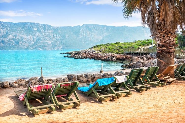 Photo of stones on the shore and wooden deck chairs on Cleopatra Island, Aegean Sea, Marmaris, Turkey.