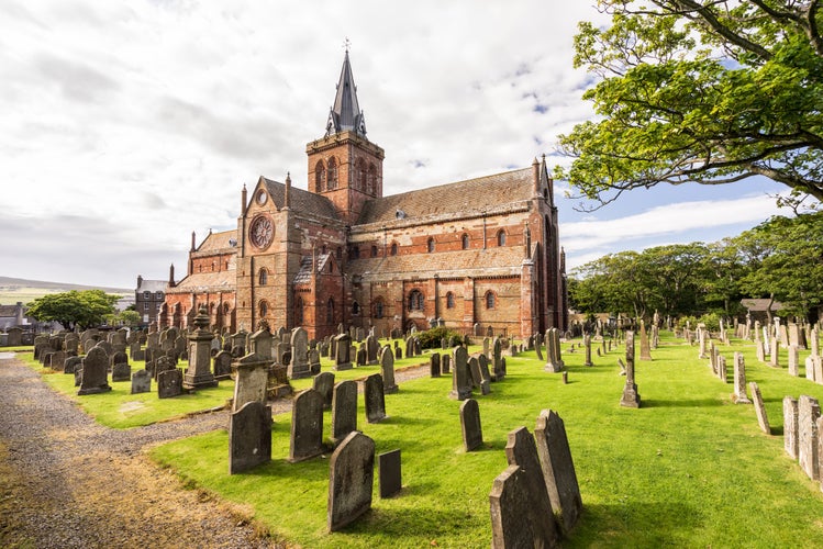 photo of St Magnus Cathedral and surrounding gothic graveyard in Kirkwall, Orkney Islands, Scotland. The holy red sandstone architecture is part of the church of Scotland.