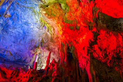 Photo of Prometheus Cave Natural Monument, Kutaisi, Georgia, with hanging stone curtains, stalactites and stalagmites, colorful illuminated rock formations.