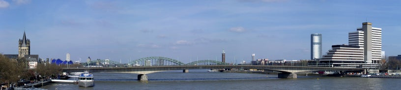 Cologne Aerial view with trains move on a bridge over the Rhine River on which cargo barges and passenger ships ply. Majestic Cologne Cathedral in the background.