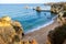 High angle view of the cliff's edge that adds a sense of height to Praia do Pinhao beach, also known as Baía dos Segredos, bathed in golden evening sun with the calm Atlantic Ocean in the background.