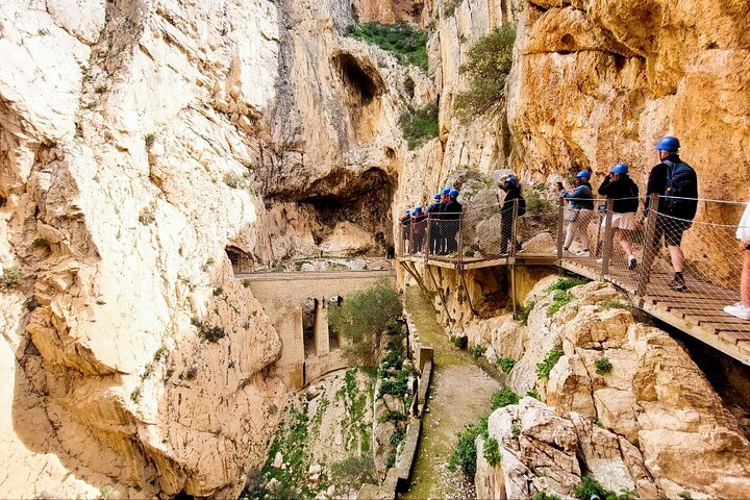 People stroll along a wooden walkway in the stunning Caminito Del Rey canyon, surrounded by towering rock formations..png