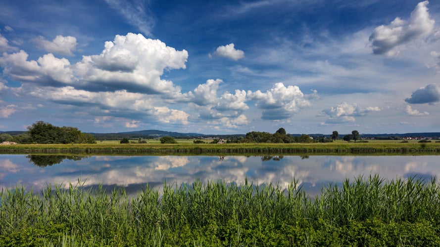 Photo of Dramatic clouds in blue sky reflect in the water of the the Rhine-Main-Danube Canal near Forchheim, Germany.