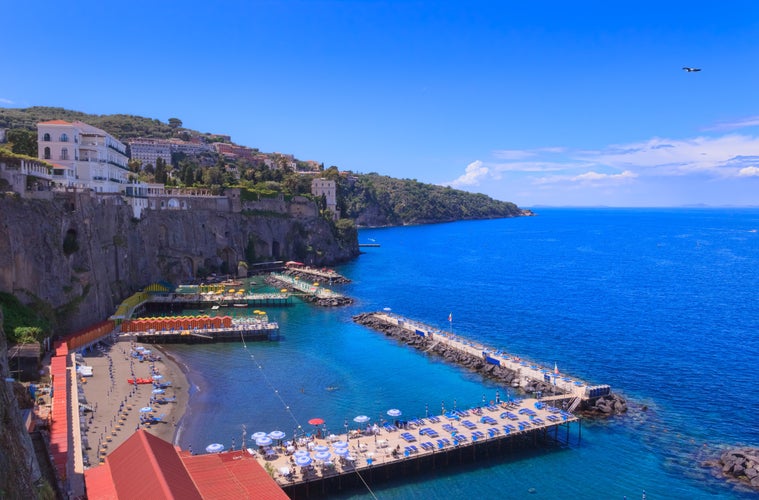 Photo of Sorrento beautiful beach in Italy with view of the jetties lined with beach huts and sun shades by the sea.