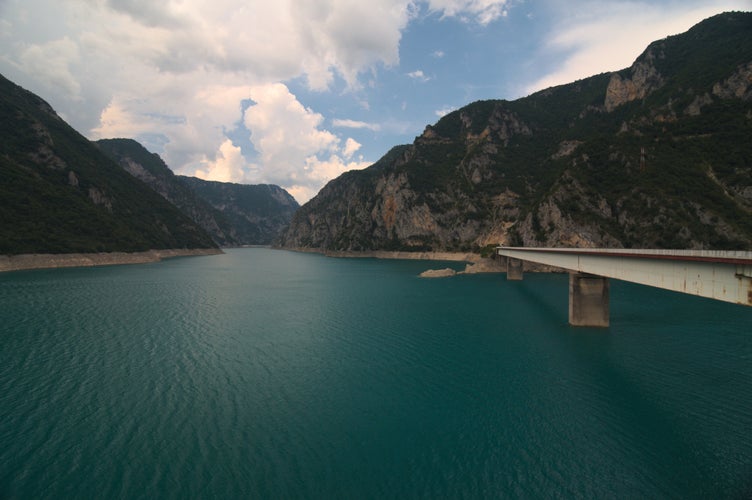 photo of view of A view into the Piva lake (Pivsko jezero) going through a valley with an old rusty bridge connecting both shores. Municipality Plužine, Montenegro.